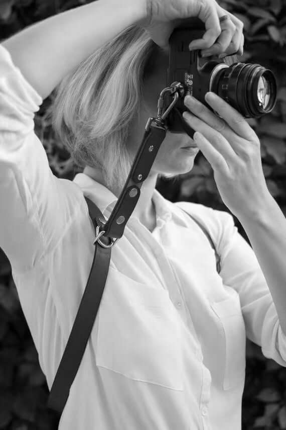Woman using a camera with a stylish leather strap, showcasing a must-have travel accessory.
