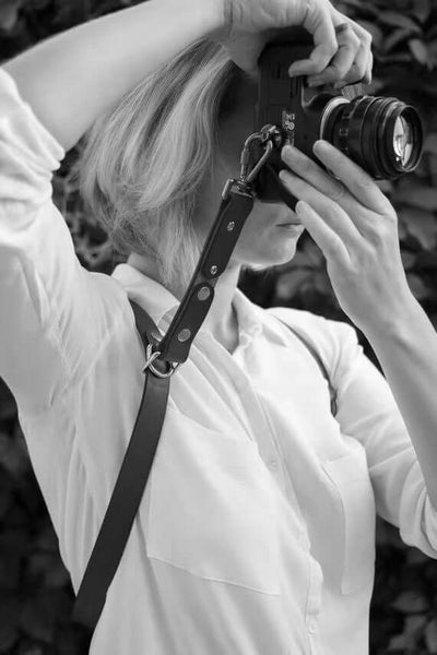 Woman using a camera with a stylish leather strap, showcasing a must-have travel accessory.