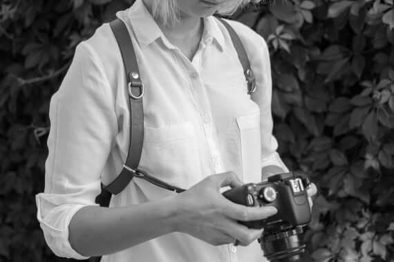 Woman wearing a stylish leather camera strap while holding a camera, perfect for travel and photography.