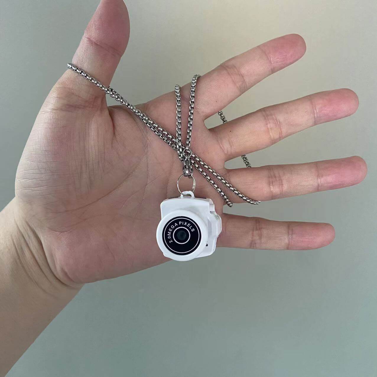 White camera necklace held in hand, stylish photography accessory with chain, ideal for camera lovers.