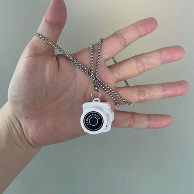 White camera necklace held in hand, stylish photography accessory with chain, ideal for camera lovers.