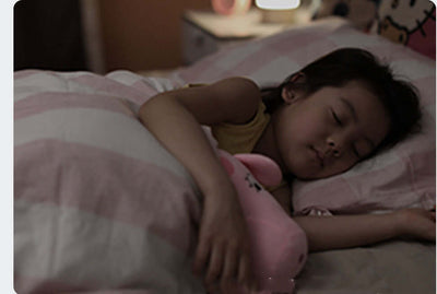 Sleeping girl cuddling a plush toy under a pink striped blanket in a cozy bedroom setting.