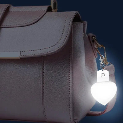 Heart-shaped LED purse lamp attached to a stylish handbag, illuminating with a soft glow.