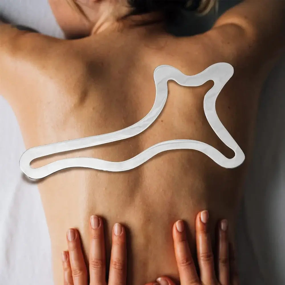 Stainless steel gua sha tool used for massage on a person's back, promoting muscle relief and lymphatic drainage.