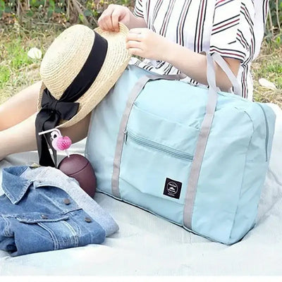 Light blue travel handbag with a front pocket displayed outdoors, alongside clothing and a hat.