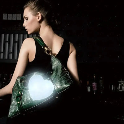 Woman with green handbag featuring a glowing heart-shaped LED light, showcasing modern purse charm accessory.
