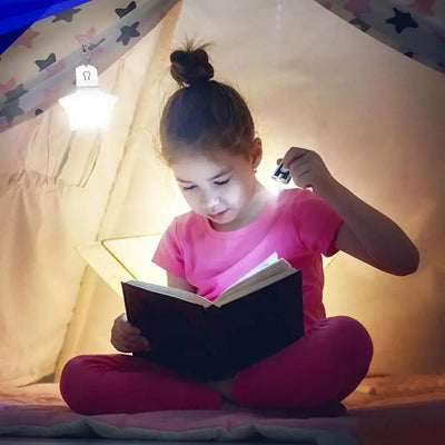 Child reading a book with a flashlight inside a cozy tent, illuminated by a hanging light.