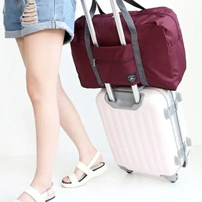 Woman carrying a burgundy travel handbag on a suitcase, showcasing its large capacity and convenient design.