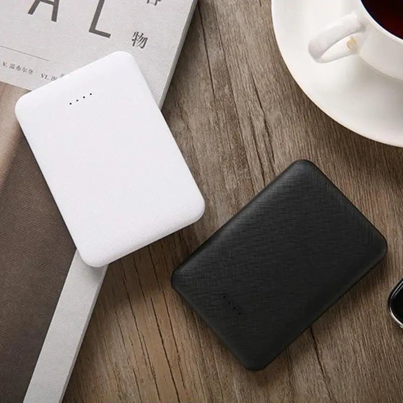 Two portable USB power banks in black and white on a wooden tabletop, next to a cup of coffee.