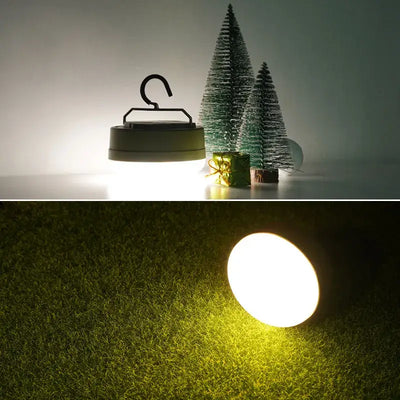 MOSLIGHTING Mini LED Camping Lantern glowing softly in a cozy outdoor setting with decorative trees.