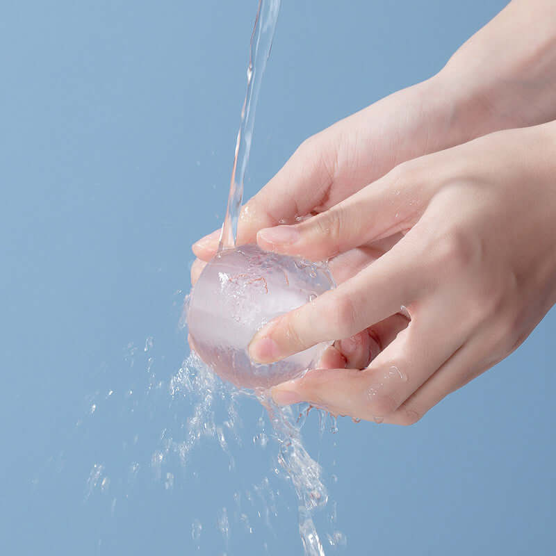 Hands holding a spherical device under running water, demonstrating its use in hair dyeing and removal.